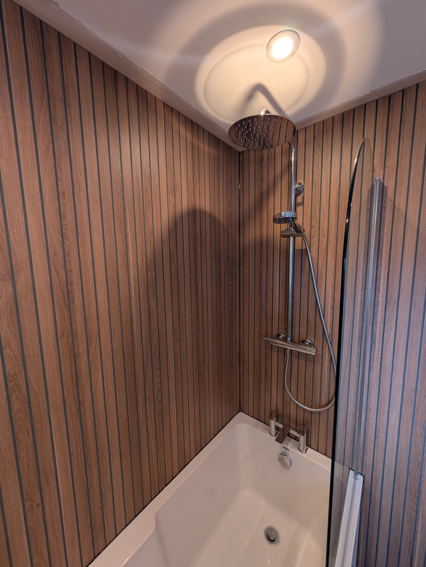 Bath with rainfall shower and oak panelling